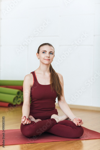 Fototapeta Naklejka Na Ścianę i Meble -  Young Woman in a red suit Doing Yoga Exercises In Gym, Sport Fitness Girl Sitting Lotus Pose Meditation Relaxation.