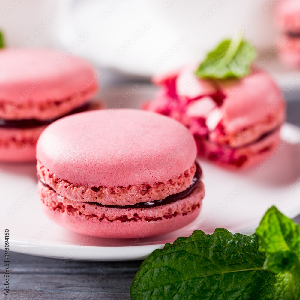 French raspberry macaroons with mint leaves on old white wooden background. Holidays food concept. French raspberry macaroons with mint leaves on old white wooden background. Holidays food concept.