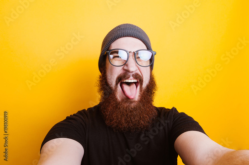 Funny cheerful bearded hipster man with eyeglasses showing tongue