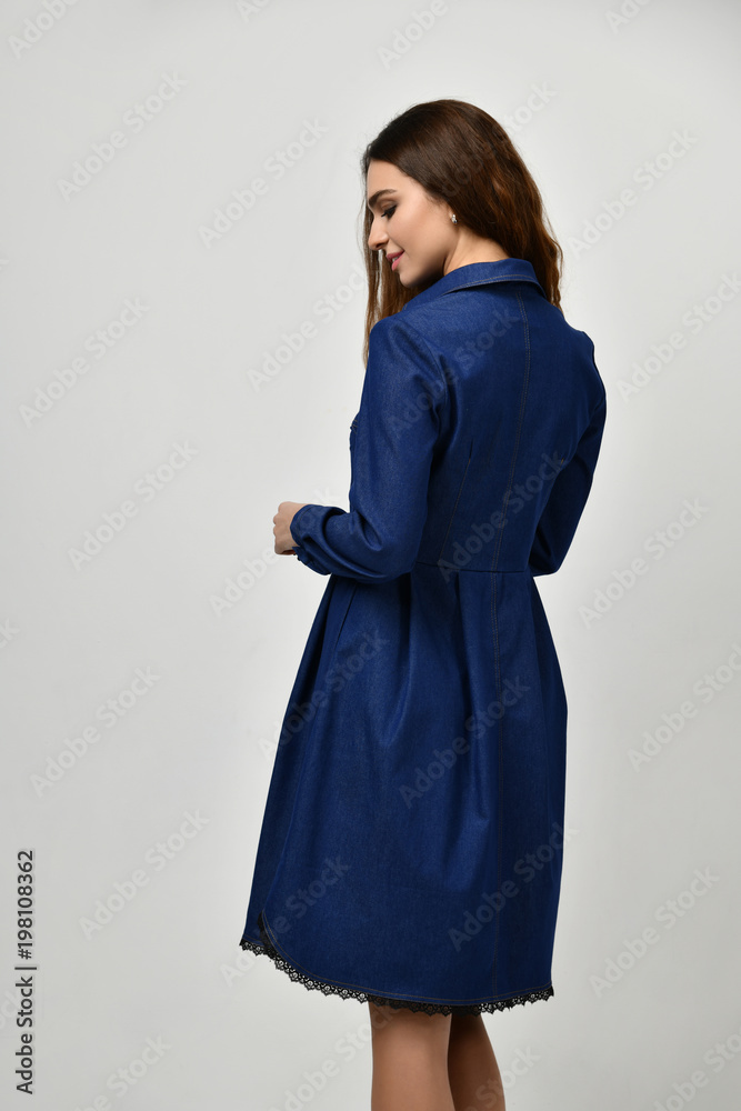Young beautiful woman posing in new casual blue jeans dress back side rear view on grey Young beautiful woman posing in new casual blue jeans dress back side rear view on grey
