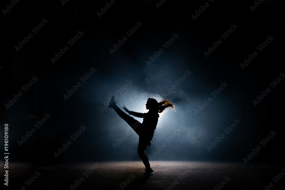 young dancer with long hair raising up her leg on dark stage. flexible girl. dancing moves.extended legs