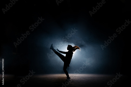 young dancer with long hair raising up her leg on dark stage. flexible girl. dancing moves.extended legs © alfa27