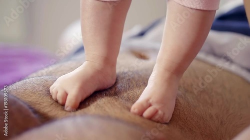 child feet are trampling on belly of father lying on bed, close up, touching moments