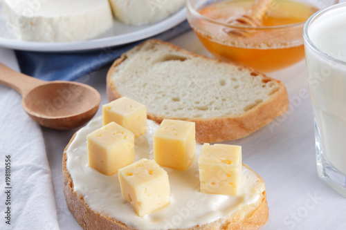 Cheese and honey on a white plate, kefir and sandwich with soft cheese, minimalism, honey and a piece of bread on the blue napkin, French breakfast on a white background, American cuisine