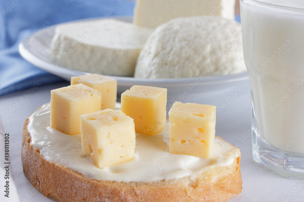 Cheese, dairy assortment on a white background, sandwich with soft cheese on a blue napkin, wooden background, wooden cutlery, white cheese on a white plate, kefir in a glass, art