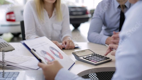 Banker Calculating Percentage To Young Couple For A Bank Loan For New Car