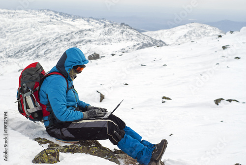 traveler working with a laptop in winter on top of a mountain during the snowfall photo