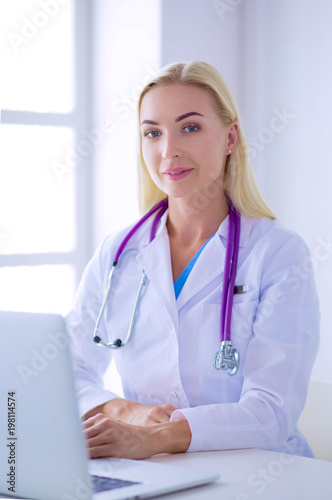 Female doctor sitting on the desk and working a laptop in hospital