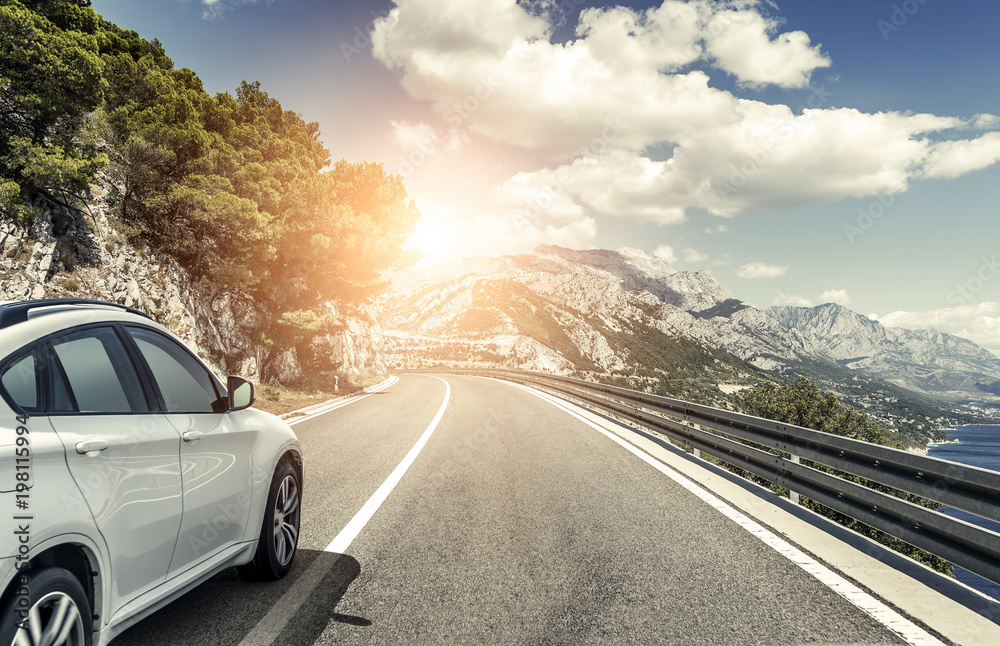 Fototapeta premium A white car rushing along a high-speed highway in the sun.