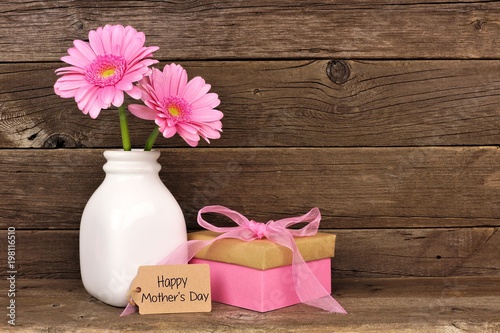 Happy Mothers Day tag with gift box and vase of pink flowers against a rustic wood background