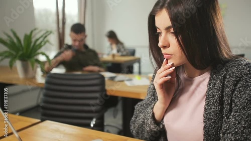 Beautiful woman in woolen gray sweater using silver computer, gets intrigued while doing different operations on the laptop, working atmosphere in it office