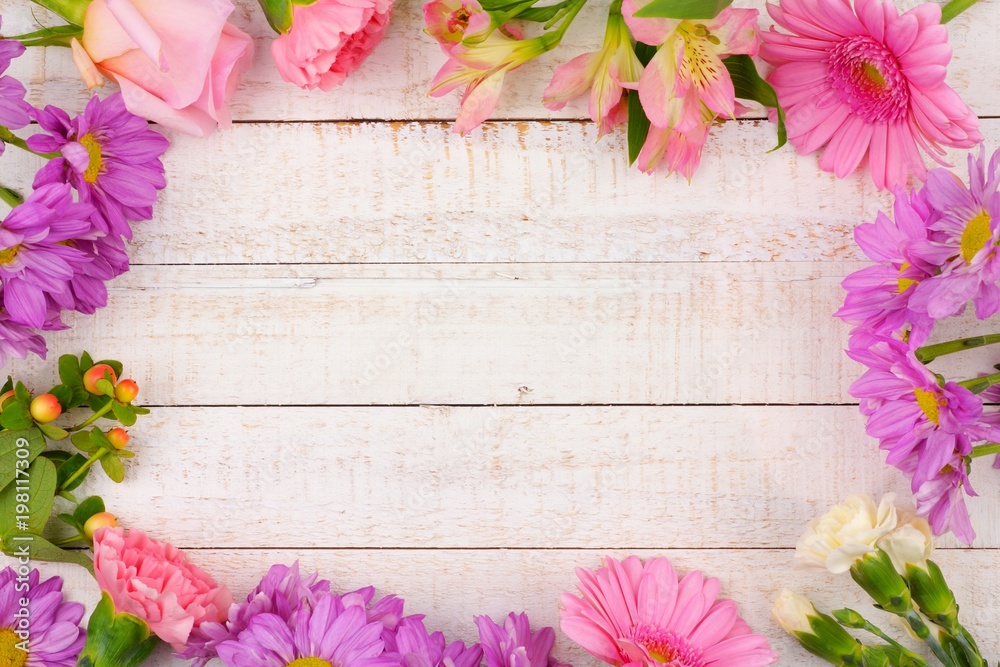 Frame of pink and purple flowers with rose, carnations, lilies and daisies against a white wood background. Copy space. Frame of pink and purple flowers with rose, carnations, lilies and daisies against a white wood background. Copy space.