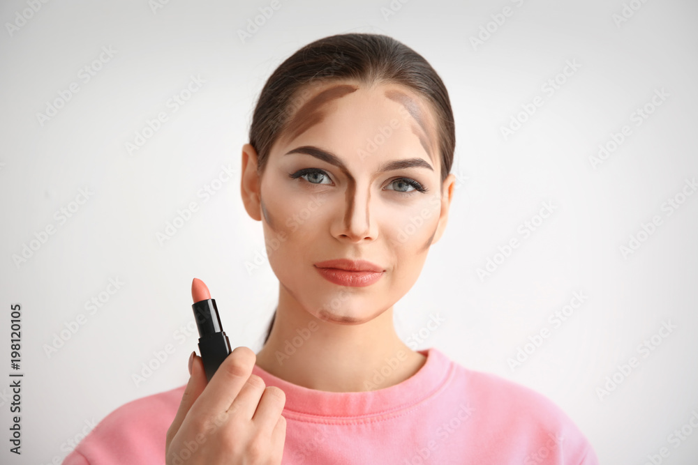 Young woman with contouring lines on her face against light background. Professional makeup products Young woman with contouring lines on her face against light background. Professional makeup products