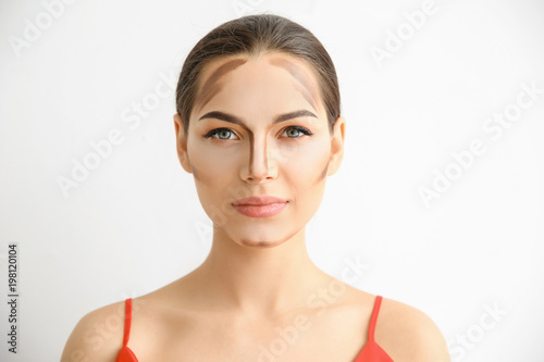 Young woman with contouring lines on her face against light background. Professional makeup products