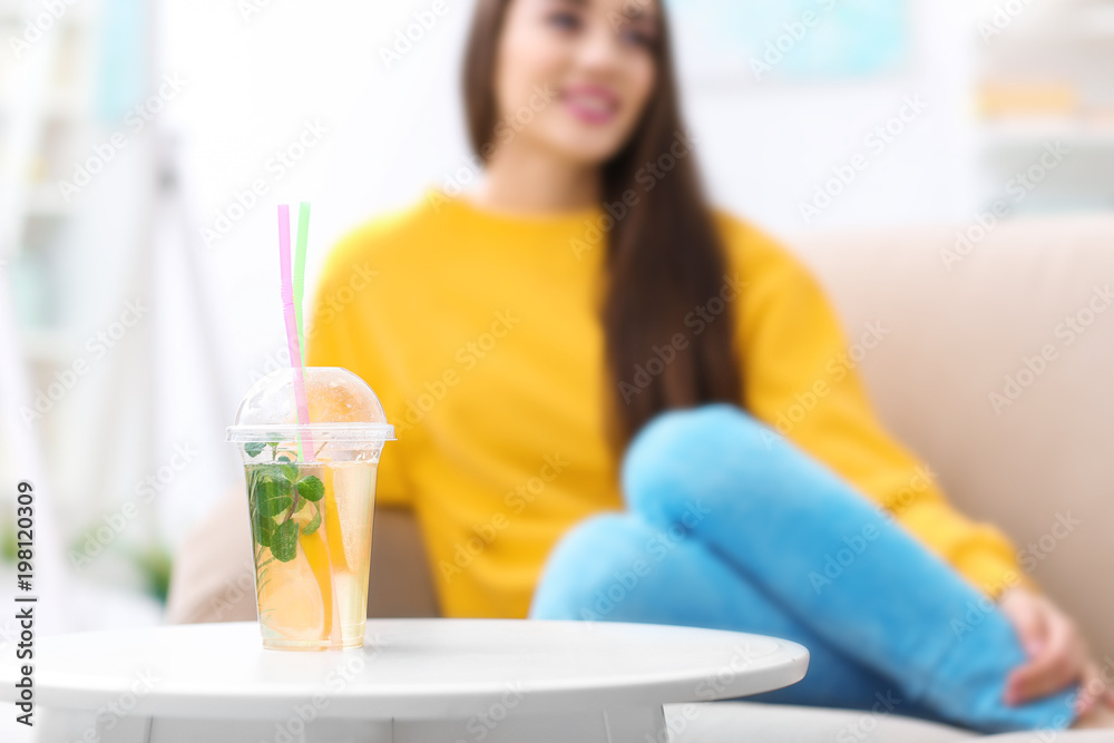 Cup with tasty refreshing lemonade and blurred woman on background Cup with tasty refreshing lemonade and blurred woman on background