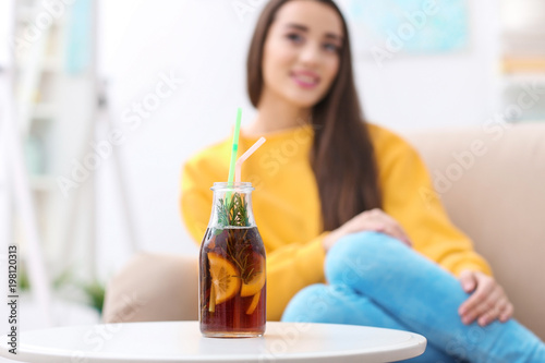 Bottle with tasty refreshing lemonade and blurred woman on background