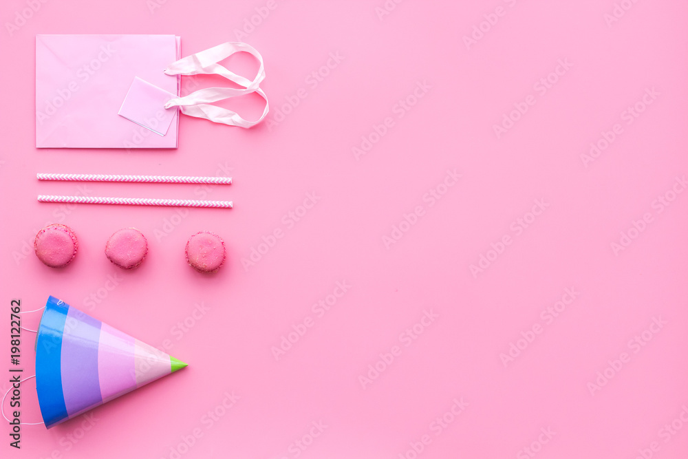 Birthday party accessories. Party hat, sweets, paper bag for gift on pink background top view copy space pattern Birthday party accessories. Party hat, sweets, paper bag for gift on pink background top view copy space pattern