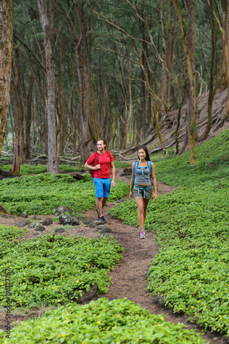 Outdoor nature people walking in forest hiking on trail path in Hawaii mountains rainforest. Happy couple with backpacks going camping with bags, enjoying landscape. Tourists on tropical travel.