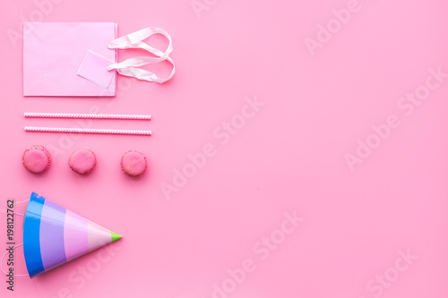 Birthday party accessories. Party hat, sweets, paper bag for gift on pink background top view copy space pattern