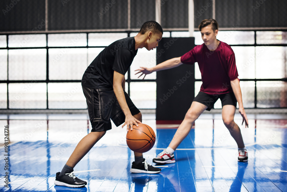 Obraz premium Two teenage boys playing basketball together on the court