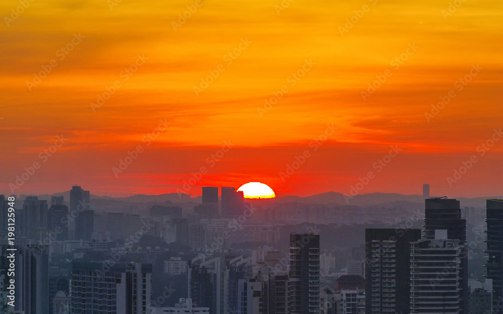 Amazing sunset in city, half of sun sink in the mountains. Fiery orange sunset sky. Beautiful sky background.