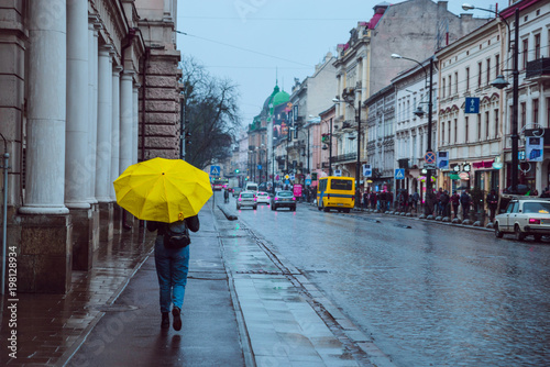 Fototapeta Naklejka Na Ścianę i Meble -  woman walk by side walk with yellow umbrella. rainy weather in old european city