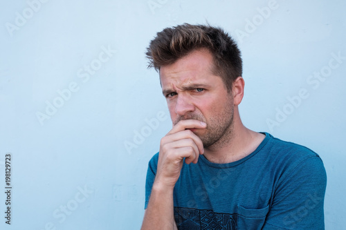 Portrait of doubtful handsome man in casual blue shirt, looking with indecisive expression on his face photo