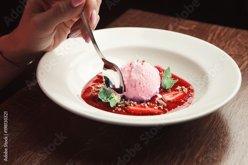 hand with spoon breaks off a slice of ice cream scoop. white dessert in plate on the table.