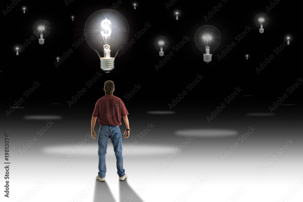 Man standing in front of a light bulb with glowing money symbol representing great money making idea, financial success and career goals, with many other dimmed idea light bulbs in the background. Man standing in front of a light bulb with glowing money symbol representing great money making idea, financial success and career goals, with many other dimmed idea light bulbs in the background.