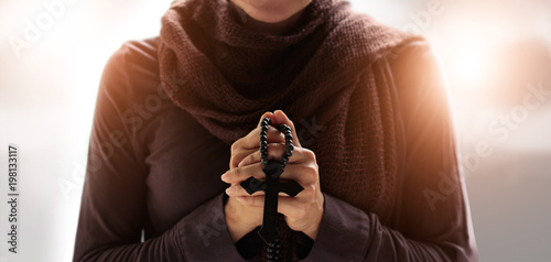 Christian Religion concept. Woman hands praying with rosary and wooden cross on soft background.