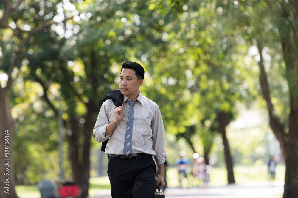 Young Asia businessman showing stress face. He was walking in the Park.. Young Asia businessman showing stress face. He was walking in the Park..