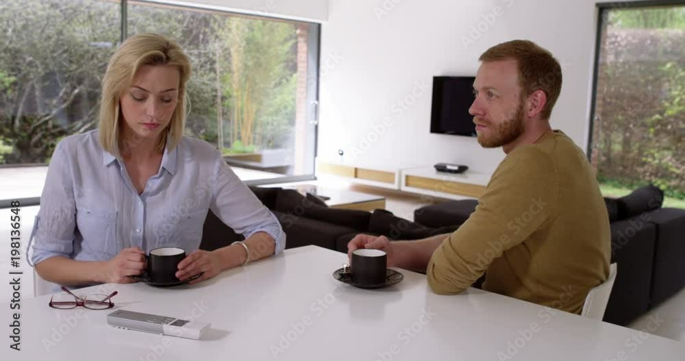 Attractive couple having awkward coffee, not speaking to each other in contemporary house, in slow motion Attractive couple having awkward coffee, not speaking to each other in contemporary house, in slow motion