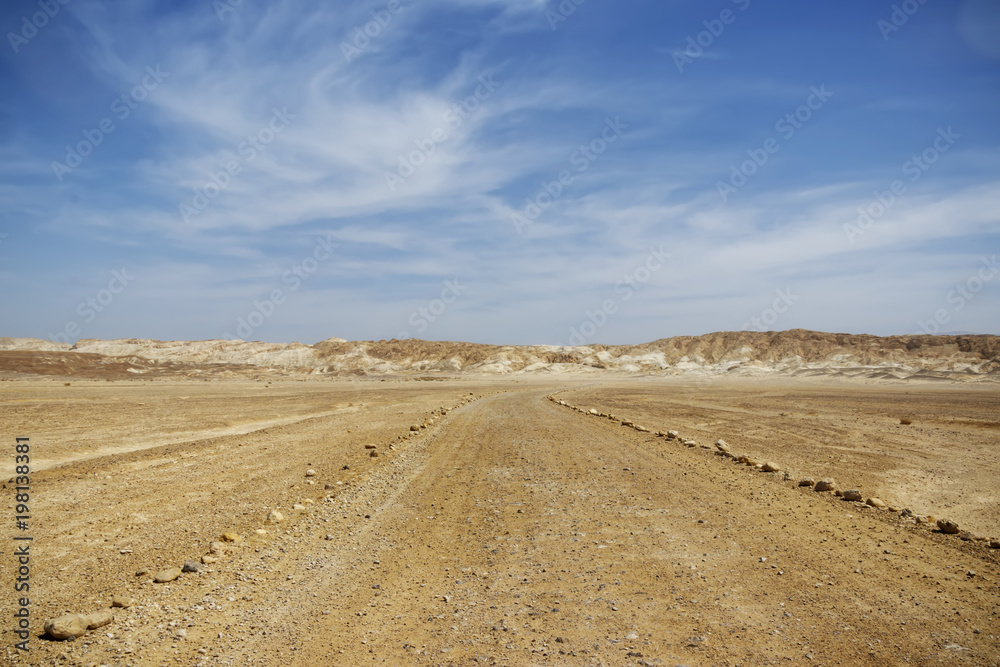 A country road in the desert of Yehuda fenced with large stones. Mountains in the background. Blue sky with clouds