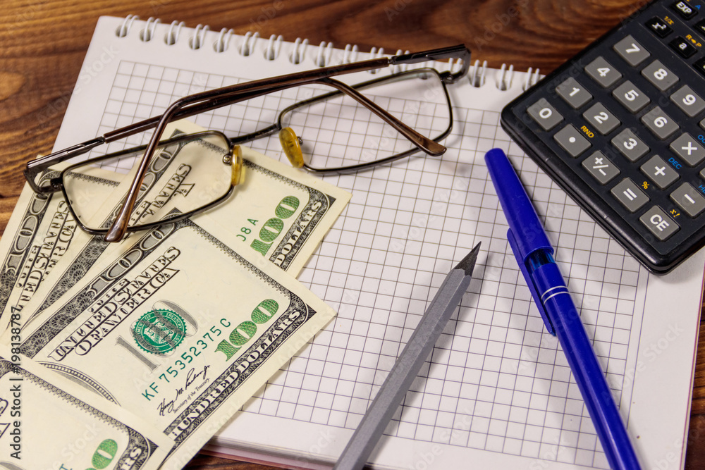 Notebook with dollars, pen, glasses and calculator on wooden desk. Financial concept. Business accounting Notebook with dollars, pen, glasses and calculator on wooden desk. Financial concept. Business accounting