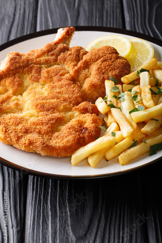 Traditional Italian veal Milanese with lemon and French fries close-up. vertical
