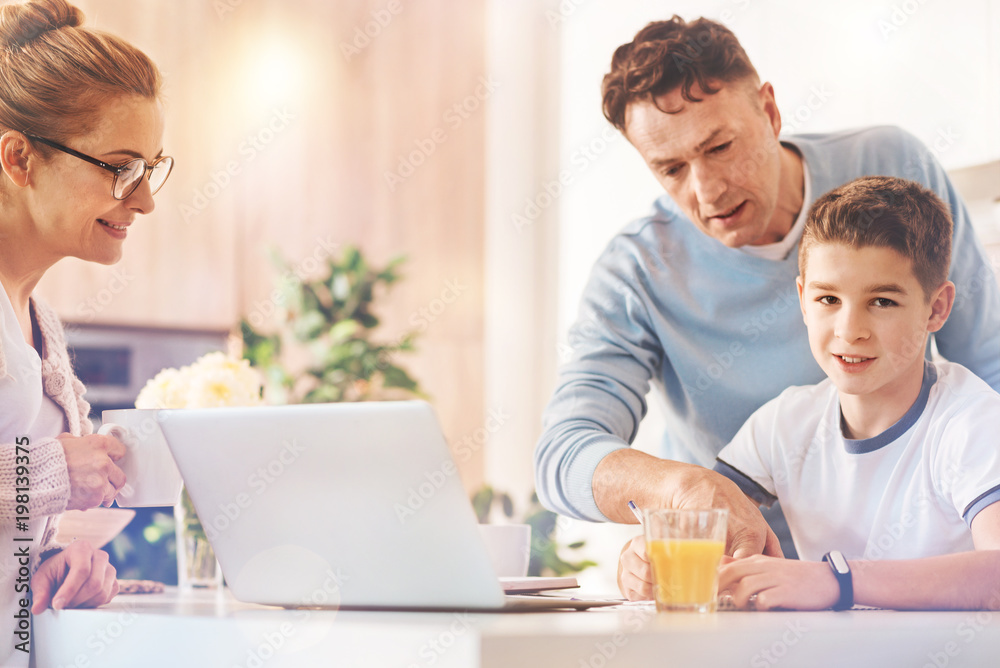 Look at this. Attentive man standing behind his son and pointing at necessary task while looking downwards Look at this. Attentive man standing behind his son and pointing at necessary task while looking downwards