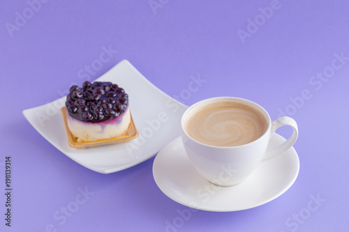 Blueberry cheesecake with coffee cup on a violet background