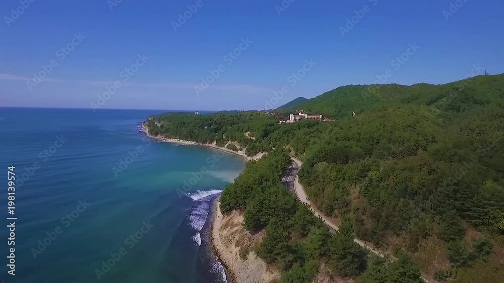 Video from the drone flying along the coast. A road passes along the shore. Blue sky. Good weather Video from the drone flying along the coast. A road passes along the shore. Blue sky. Good weather