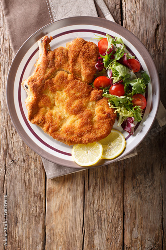 veal Milanese with lemon and fresh salad of tomatoes and lettuce close-up. Vertical top view