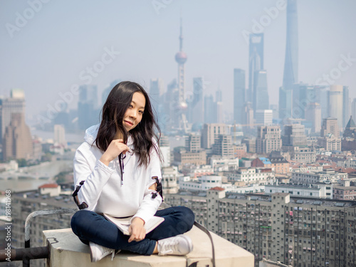Canvas Print Beautiful young brunette woman sit on top of mansion roof with blur Shanghai Bund landmark buildings background