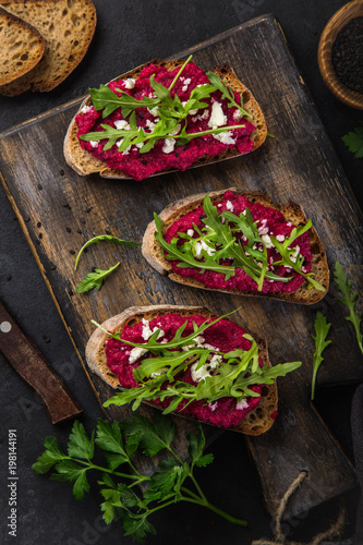 toasts with beetroot hummus, feta cheese and arugula on cutting board