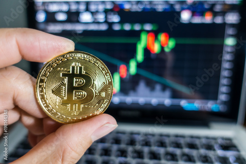 Businessman holding Golden Bitcoin in front of laptop with stock exchange graph background. Digital money concept. photo