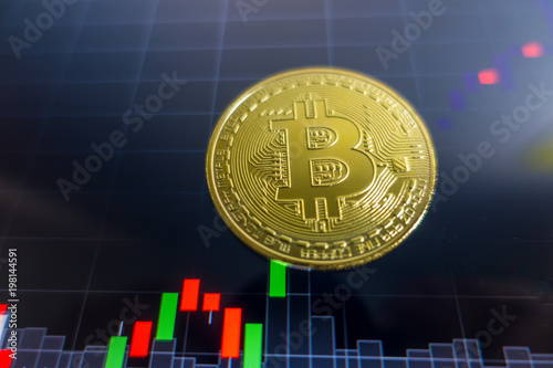 Golden Bitcoin on black laptop screen with stock exchange graph background. Digital money concept.