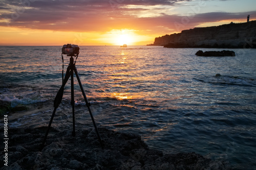 Camera on a tripod on the sea beach during a beautiful fiery sunset