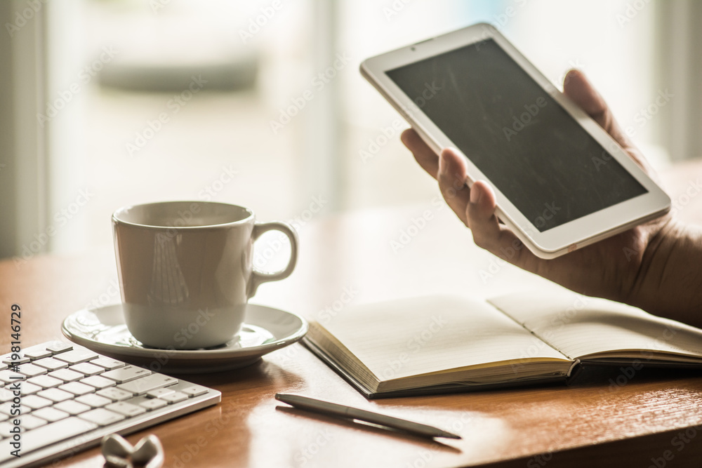 Businessman hand holding a tablet computer with coffee cup ,smart phone and keyboard on office table. Businessman hand holding a tablet computer with coffee cup ,smart phone and keyboard on office table.