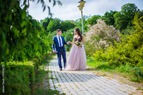 Bride and groom holding hands and walking in park in summer