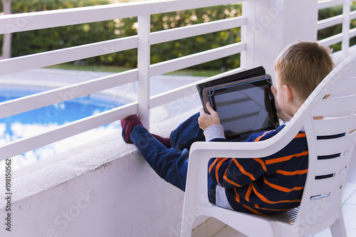 cute little boy is playing in the tablet on the balcony on a vacation in the spring photo