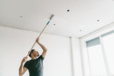the man paints the ceiling in a gray color with a roller in a bright room. Repair and painting.