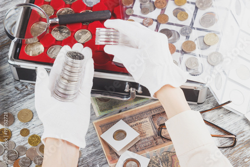 Hands in the white gloves with different collector coins in the boxes