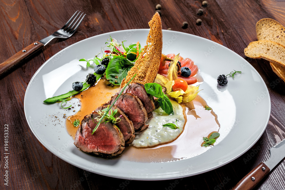 Gourmet medium rare meat steak with sauce and fresh salad. Healthy meal made of meat fillet and fresh vegetables on a rustic table. Gourmet medium rare meat steak with sauce and fresh salad. Healthy meal made of meat fillet and fresh vegetables on a rustic table.